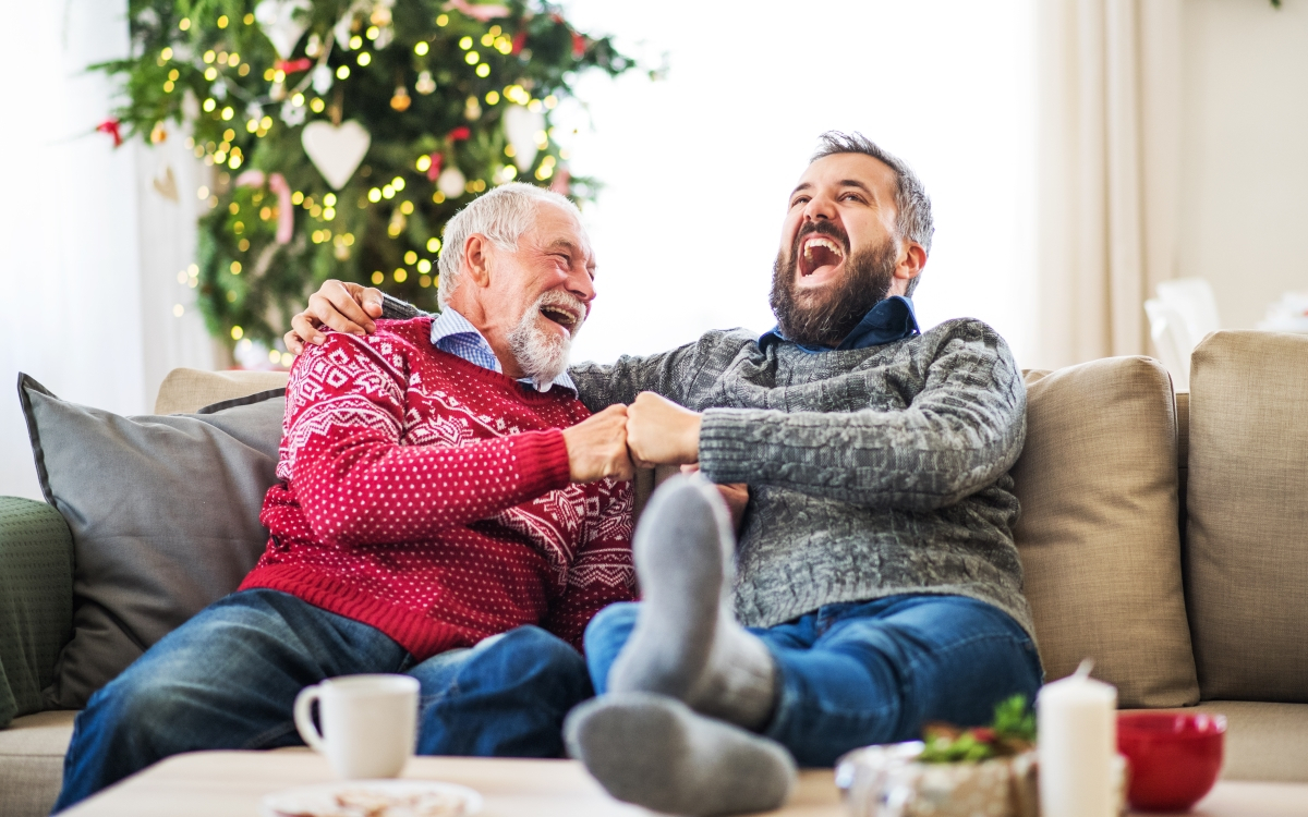 Vater und Sohn sitzen an Weihnachten auf dem Sofa und lachen herzhaft