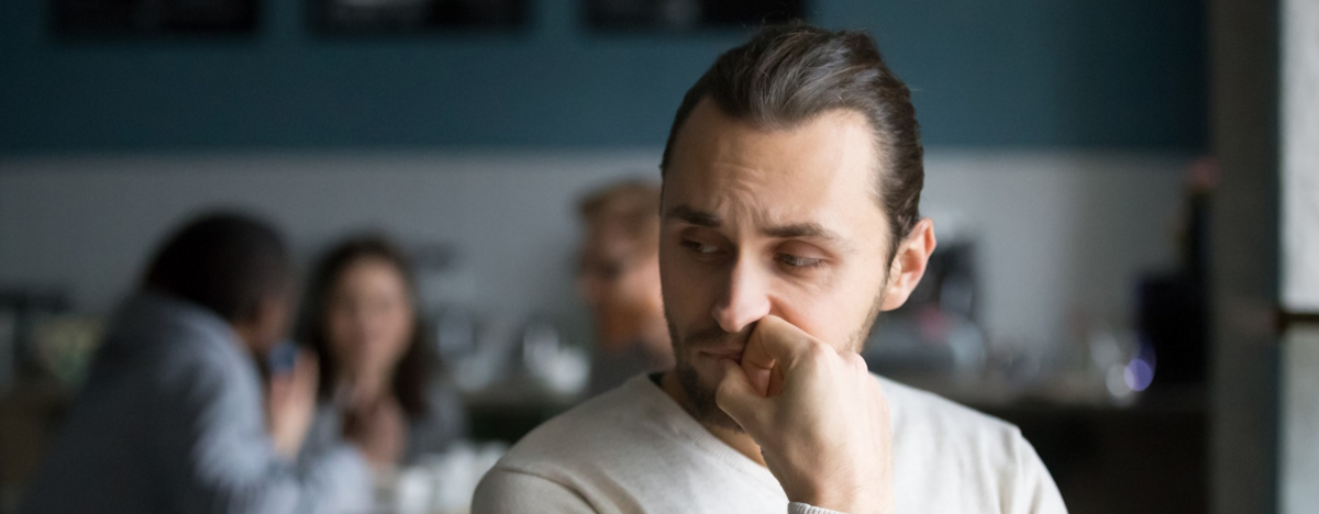Genervter Mann sitzt allein mit abweisender Haltung im Cafe