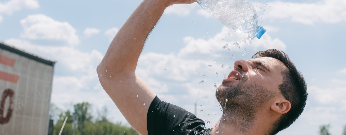 Mann sch&uuml;ttet sich Wasser aus einer Plastikflasche &uuml;ber den Kopf