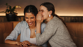 Eine Frau fl&uuml;stert ihrer Freundin etwas ins Ohr