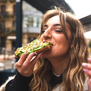Eine junge Frau bei&szlig;t gen&uuml;sslich in ein Brot mit Avocado.