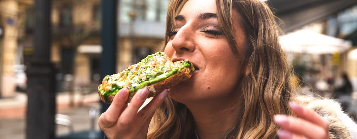 Eine junge Frau bei&szlig;t gen&uuml;sslich in ein Brot mit Avocado.