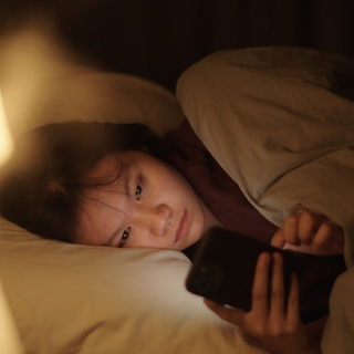 Ein asiatisches M&auml;dchen liegt im Bett und schaut auf ihr Smartphone.