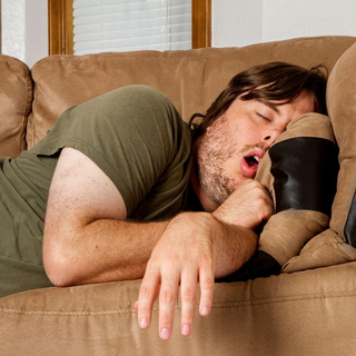 Ein Mann schl&auml;ft und prokrastiniert auf dem Sofa.