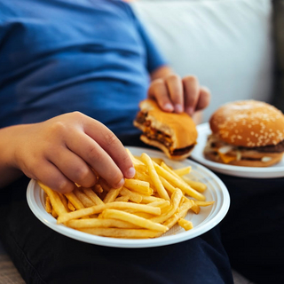 Eine kindliche Hand greift nach Pommes und Burger.