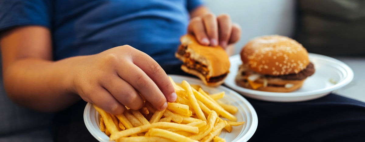 Eine kindliche Hand greift nach Pommes und Burger.