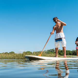 Paar gleitet auf Paddelboards stehend auf einem See entlang