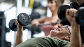 Ein Mann trainiert mit Hanteln, ein anderer Mann unterst&uuml;tzt ihn dabei