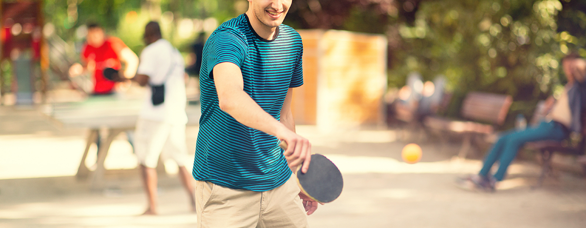 Junger Mann spielt drau&szlig;en Tischtennis an einer Tischtennisplatte