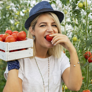 Junge blonde Frau isst eine frische Tomate im Garten.