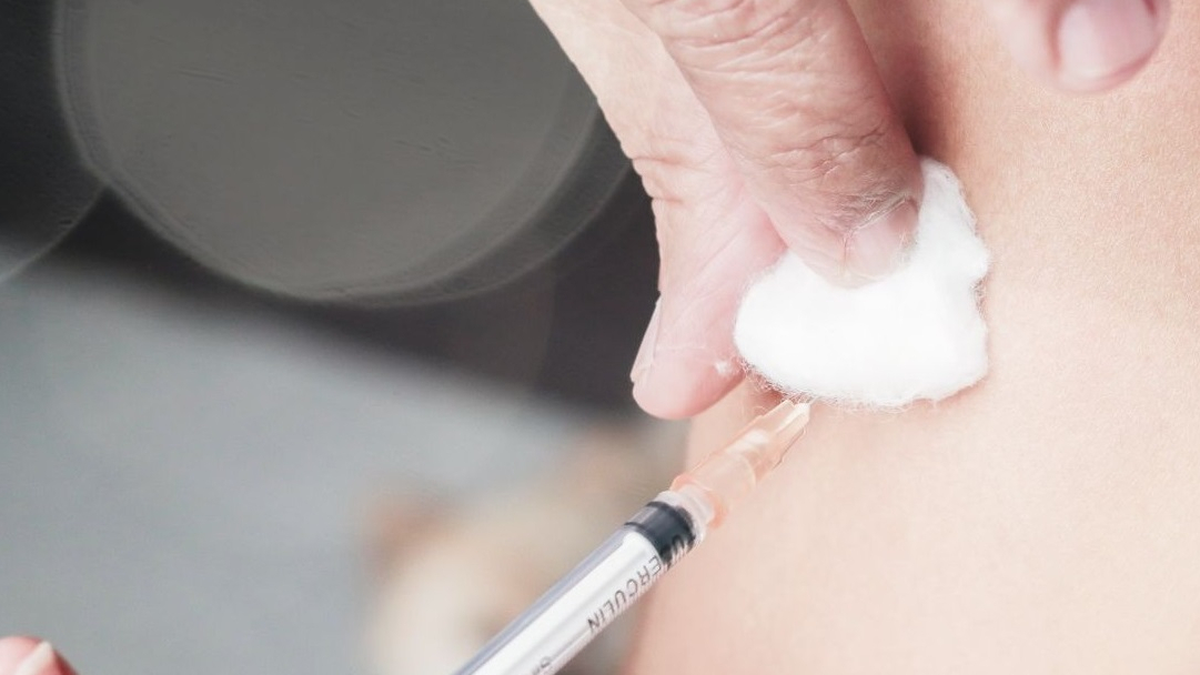 Nahaufnahme Spritze im Arm mit Wattepad