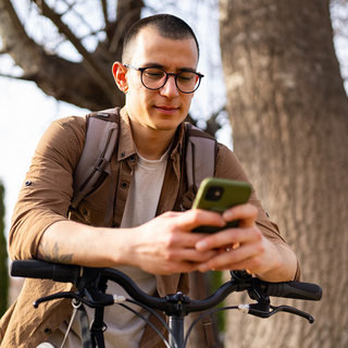 Junger Mann benutzt Handy und steht neben seinem Fahrrad drau&szlig;en.