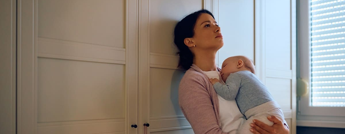 Junge traurige Mutter, die ihr schlafendes Baby zu Hause in den Armen h&auml;lt.