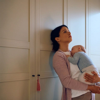 Junge traurige Mutter, die ihr schlafendes Baby zu Hause in den Armen h&auml;lt.