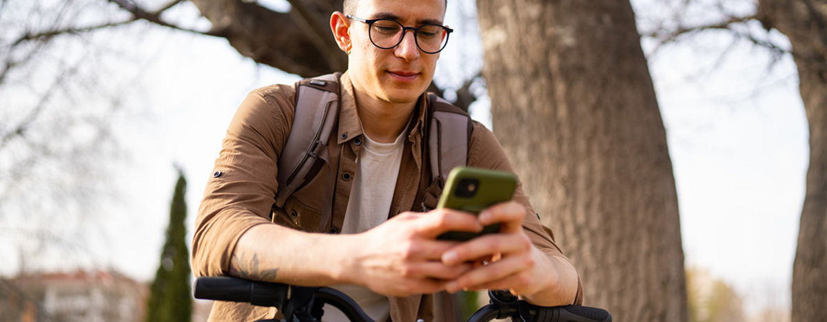 Junger Mann benutzt Handy und steht neben seinem Fahrrad drau&szlig;en.
