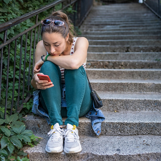 Eine traurige Frau sitzt auf einer Treppe und starrt auf ihr Smartphone.