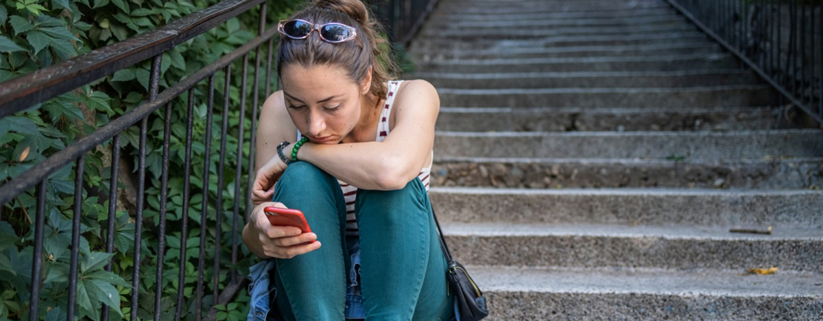 Eine traurige Frau sitzt auf einer Treppe und starrt auf ihr Smartphone.