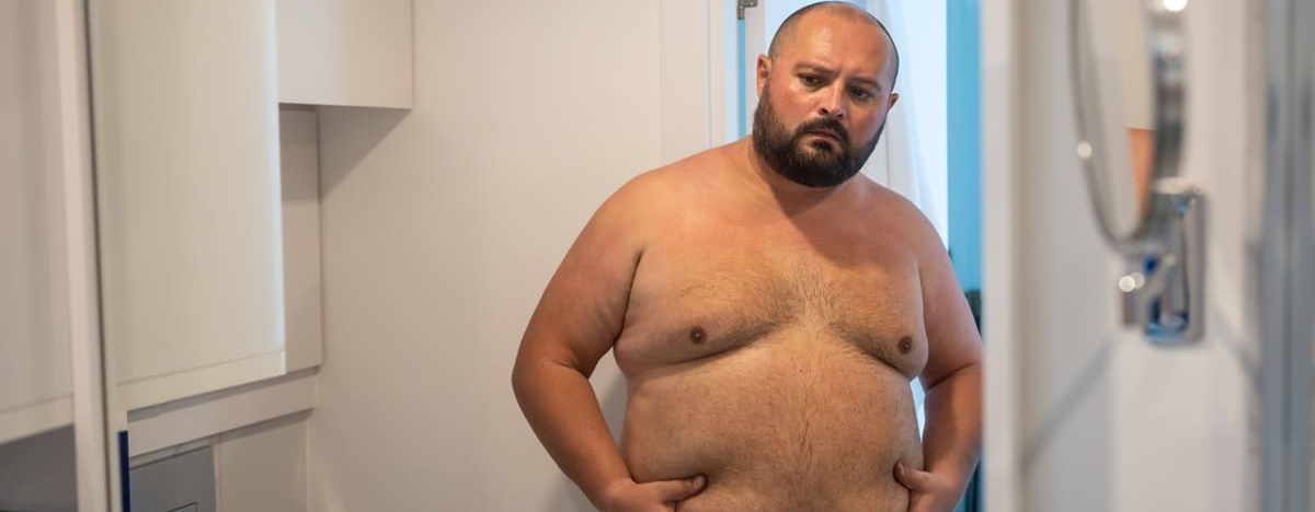 &Uuml;bergewichtiger Mann, der den Bauch vor dem Spiegel ber&uuml;hrt, unzufrieden mit &Uuml;bergewicht, besorgt &uuml;ber die Figur