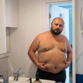 &Uuml;bergewichtiger Mann, der den Bauch vor dem Spiegel ber&uuml;hrt, unzufrieden mit &Uuml;bergewicht, besorgt &uuml;ber die Figur