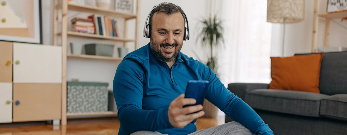 Mann sitzt auf einer Yogamatte und l&auml;chelt in sein Handy