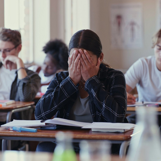 Eine Jugendliche sitzt im Klassenzimmer, verbirgt ihr Gesicht in den H&auml;nden wegen Pr&uuml;fungsangst.