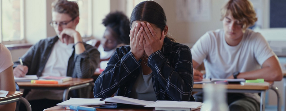 Eine Jugendliche sitzt im Klassenzimmer, verbirgt ihr Gesicht in den H&auml;nden wegen Pr&uuml;fungsangst.