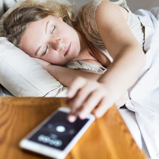 Junge Osteurop&auml;ische Frau liegt im Bett und schaltet morgens den Wecker auf ihrem Handy aus