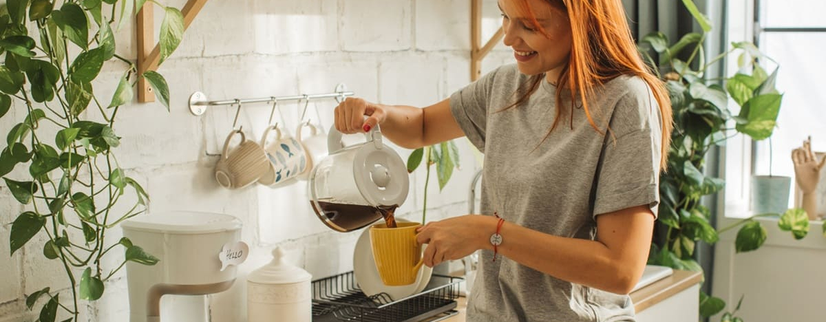 Eine junge Frau f&uuml;llt Kaffee aus einer Filtermaschine in eine Tasse.