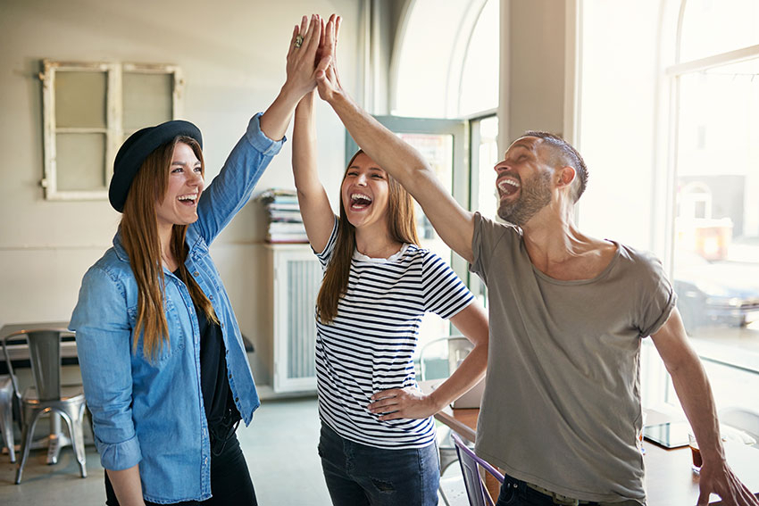 Drei junge Menschen beim fr&ouml;hlichen Abklatschen in einem B&uuml;ro
