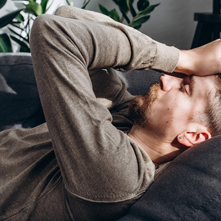 Mann liegt auf dem Sofa und h&auml;lt sich schmerzerf&uuml;llt die H&auml;nde an den Kopf