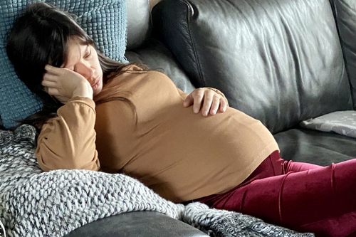 schwangere Frau liegt ersch&ouml;pft auf der Couch