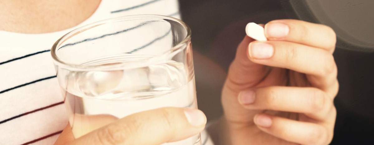 Eine Frau h&auml;lt ein Glas mit Wasser und eine Tablette in den H&auml;nden