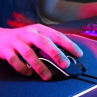 Gamer mit moderner kabelgebundener Computermaus in Neonlichtern am dunklen Tisch, Nahaufnahme