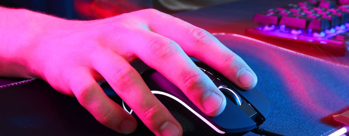 Gamer mit moderner kabelgebundener Computermaus in Neonlichtern am dunklen Tisch, Nahaufnahme