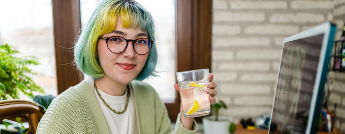 Eine junge Frau sitzt am Computer und trinkt Zitronenwasser.