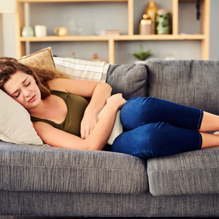 Junge Frau mit Magenkr&auml;mpfen liegt auf Sofa.