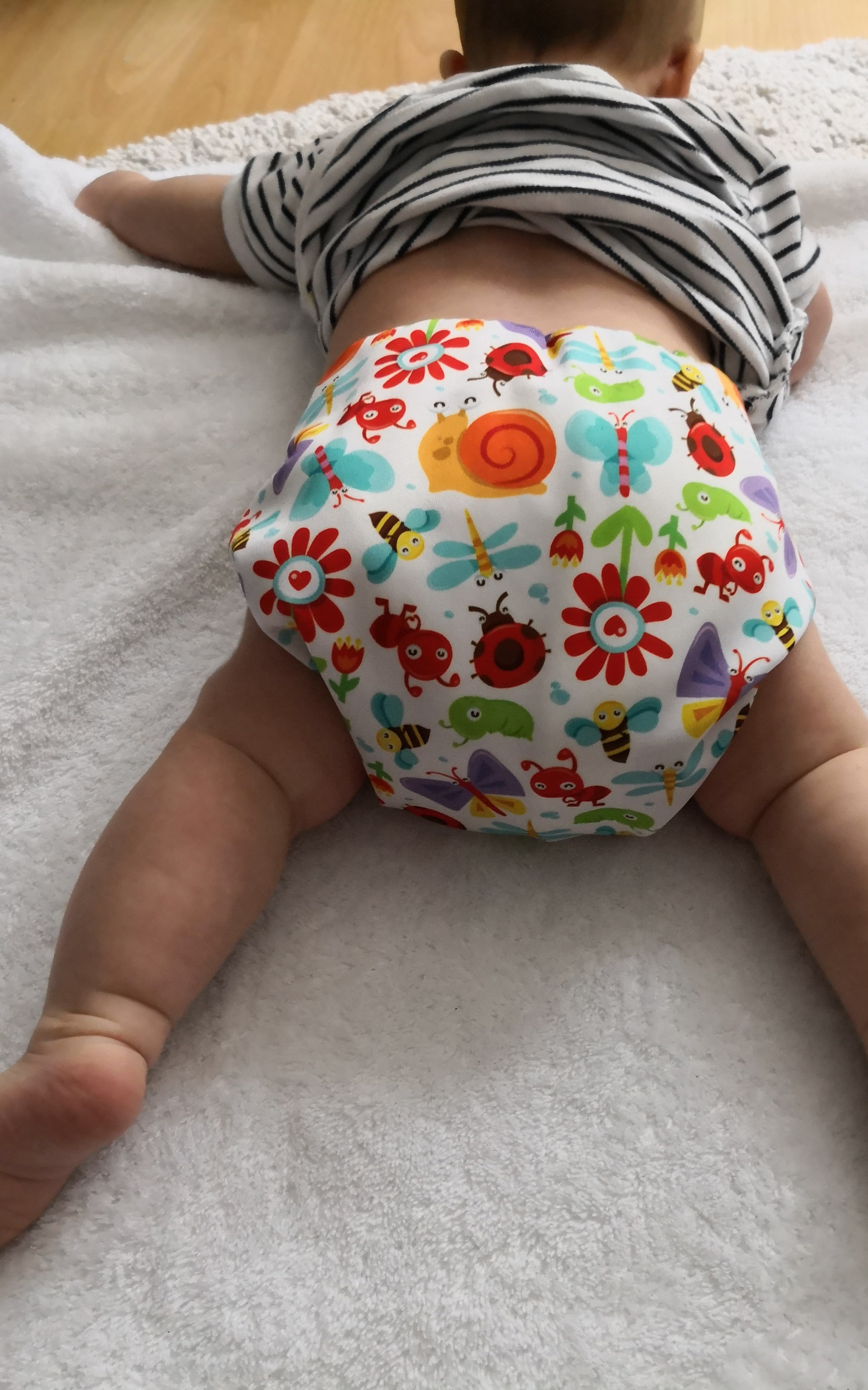 Ein auf dem Boden liegendes Baby, das eine bunte Stoffwindel tr&auml;gt