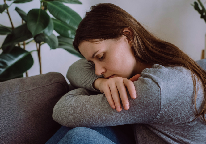 Depressive traurige junge Frau, die auf der Couch im Wohnzimmer sitzt