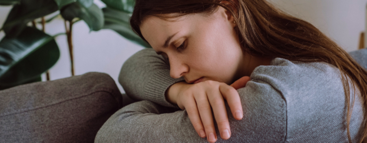 Depressive traurige junge Frau, die auf der Couch im Wohnzimmer sitzt