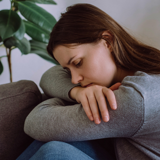 Depressive traurige junge Frau, die auf der Couch im Wohnzimmer sitzt