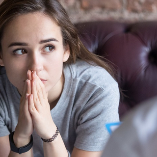 Eine ungl&uuml;ckliche junge Frau sitzt auf einem Sofa gegen&uuml;ber eines Therapeuten.