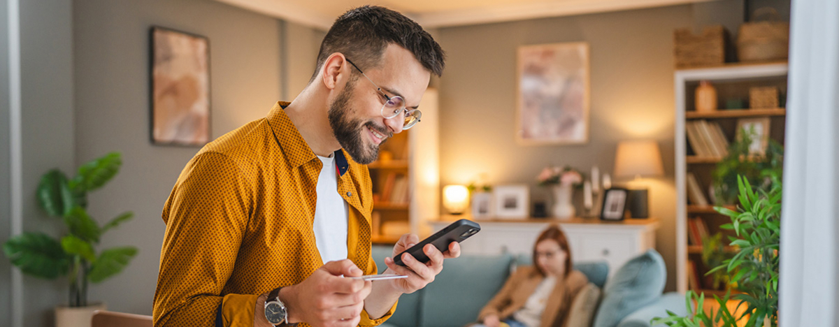 Junger Mann schaut auf sein Handy und h&auml;lt seine Gesundheitskarte in der Hand