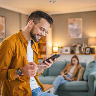 Junger Mann schaut auf sein Handy und h&auml;lt seine Gesundheitskarte in der Hand