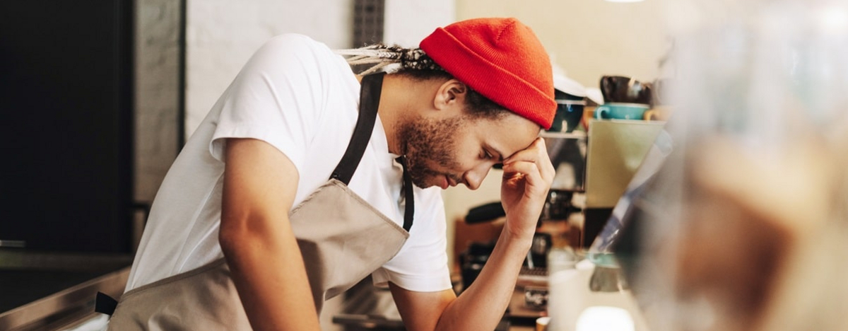 Junger lateinamerikanischer Barista, der sich bei der Arbeit im Caf&eacute; gestresst f&uuml;hlt.