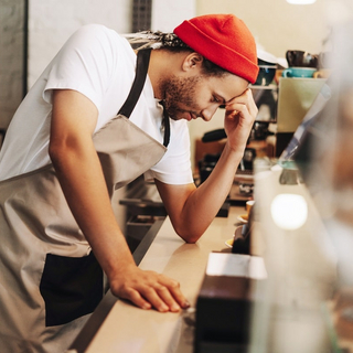 Junger lateinamerikanischer Barista, der sich bei der Arbeit im Caf&eacute; gestresst f&uuml;hlt.