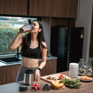 Nahaufnahme einer sportlichen Frau, die einen Proteinshake trinkt, in ihrer K&uuml;che.