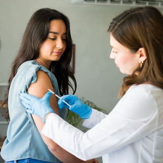 Mediziner mit Handschuhen verabreicht einer jungen Frau in einer Arztpraxis einen Impfstoff