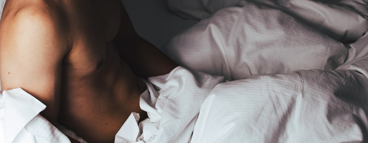Nackte schlanke Muskel Mann im Bett mit wei&szlig;en Laken bedeckt liegen