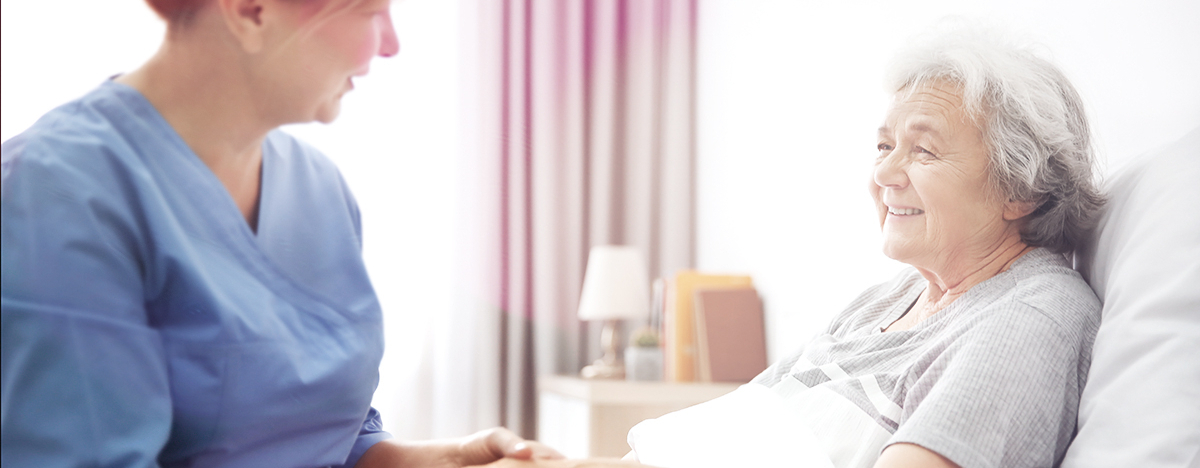 Eine Pflegerin h&auml;lt die Hand einer &auml;lteren, pflegebed&uuml;rftigen Frau im Bett