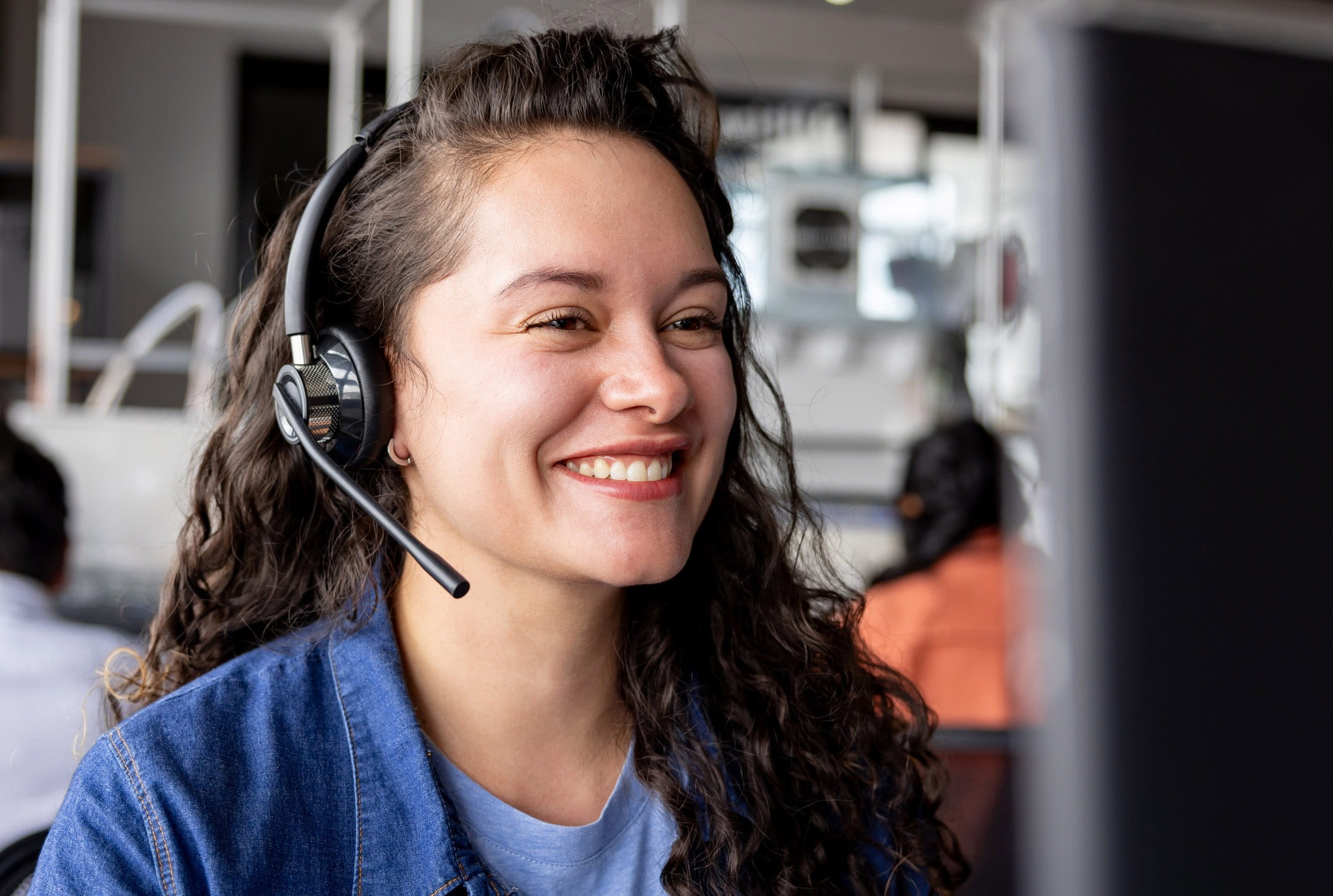 Eine junge Frau mit lockigen Haaren tr&auml;gt ein Headset, arbeitet im Kundendienst.